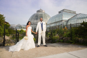 Bride and groom holding hands by glass conservatory